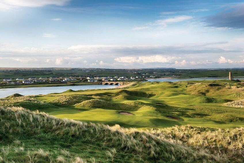 A golf course with rolling green hills, a water body, and a distant town. 4