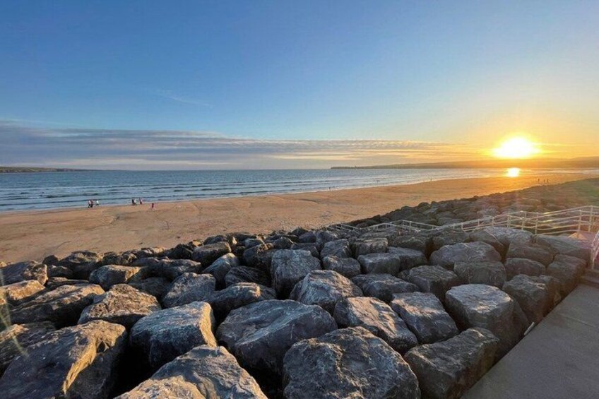 A beach with large rocks in the foreground and the sun setting over the ocean. 2