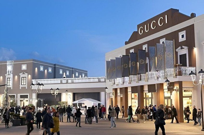 Ein belebter Stadtplatz mit einem markanten GUCCI Geschäft und weiteren Einzelhandelsgeschäften. 4