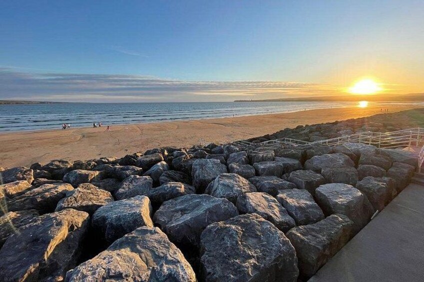 A beach with large rocks in the foreground and the sun setting in the background. 3