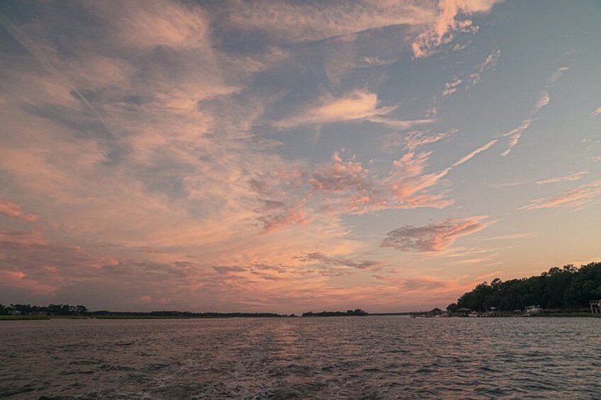 Een zonsondergang boven een wateroppervlak met een verre kustlijn en een bewolkte lucht. 5