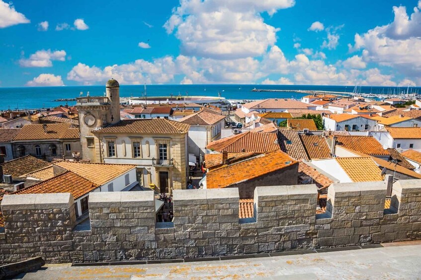A coastal town with historic stone walls, terracotta-roofed buildings, and a clear blue sky. 3