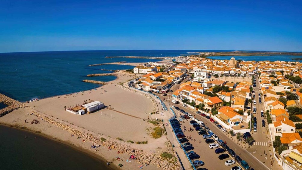 A coastal town with a beach, a church, and a road lined with orange-roofed buildings. 1