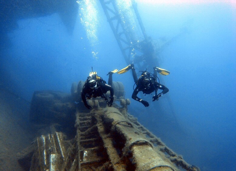 Two scuba divers underwater near a large metal structure. 1
