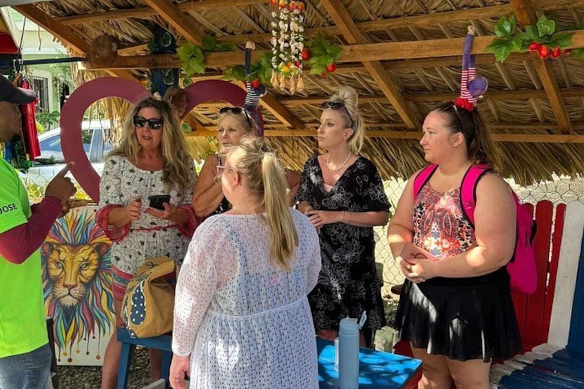 A group of people under a thatched roof structure with a lion mural, engaged in conversation. 1