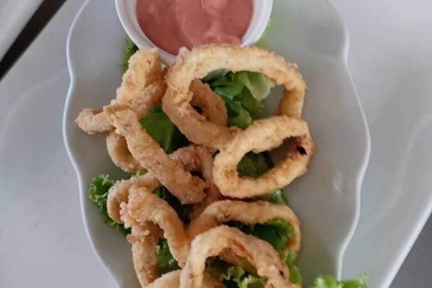 A plate of fried calamari rings with a side of dipping sauce and lettuce. 3