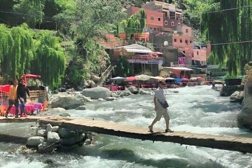 Ein Fluss mit einer Holzbrücke, Spaziergänger und Gebäude im Hintergrund. 5