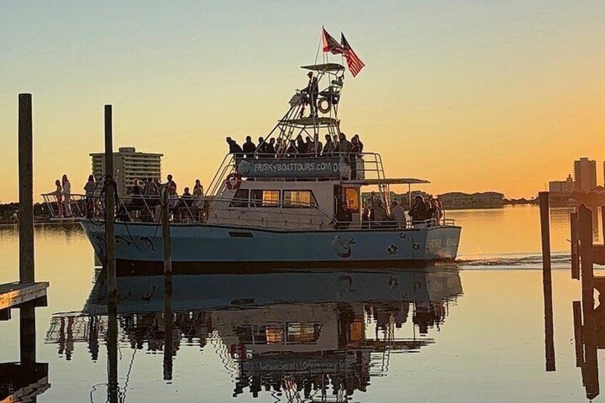 A boat docked at a pier with people on board, a flag, and a calm water body reflecting the surroundings. 3