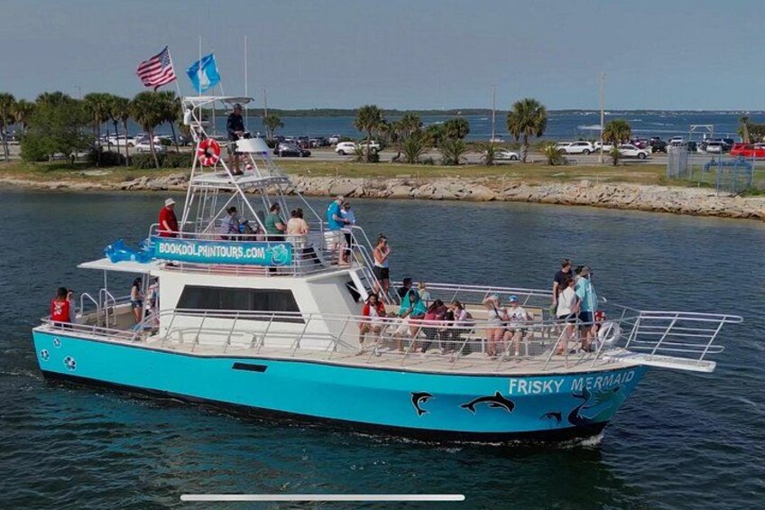 Un bateau de tourisme appelé « Frisky Mermaid », transportant des passagers, une bannière de site web et un cadre paisible au bord de l’eau. 3