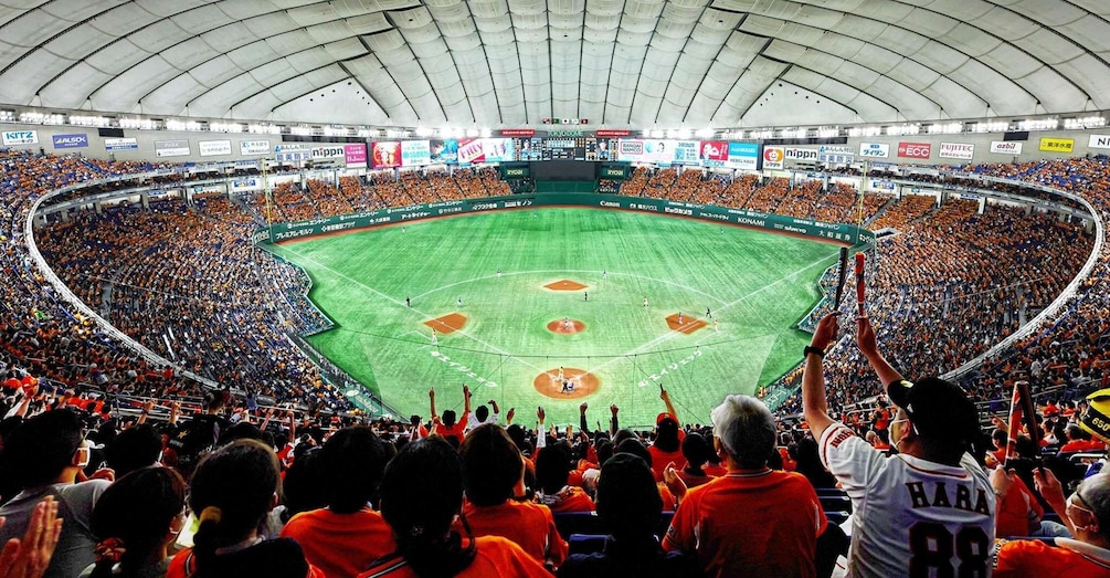 A baseball stadium filled with spectators, a baseball diamond, and advertisements on the stadium walls. 1