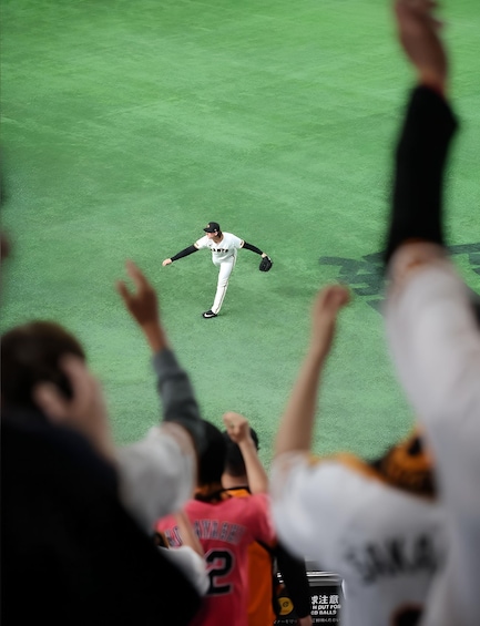 A baseball player in a white uniform pitching on a field with spectators in the foreground. 3