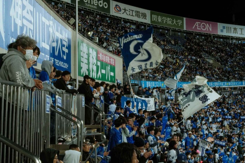 A crowded stadium with fans holding banners and flags, and advertisements on the stands. 2