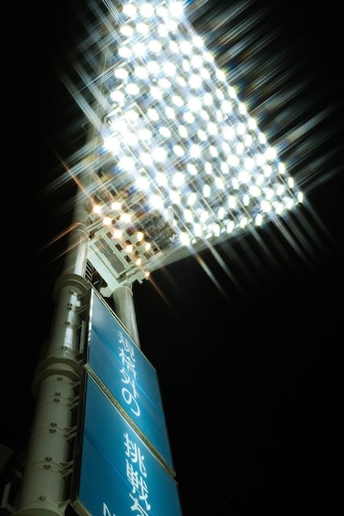 A night scene with a brightly lit street lamp and a blue sign with white text. 4