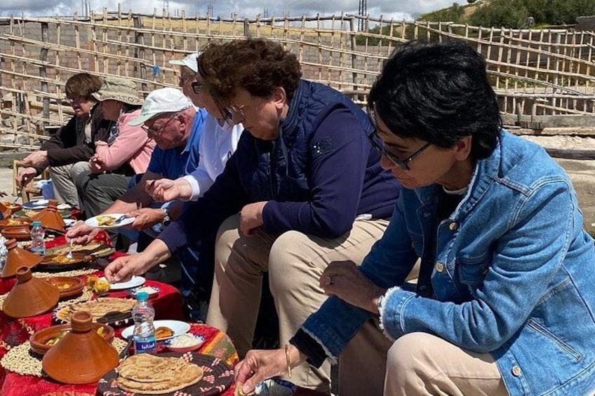 People sitting at a table with food and drinks, outdoors with a wooden structure in the background. 4