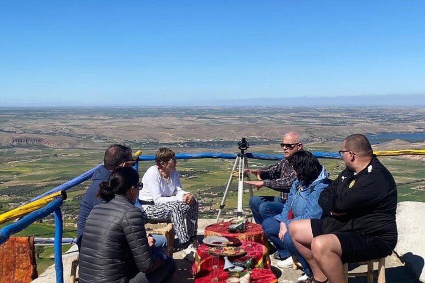 A group of people sitting on a platform with a camera on a tripod, overlooking a landscape. 1