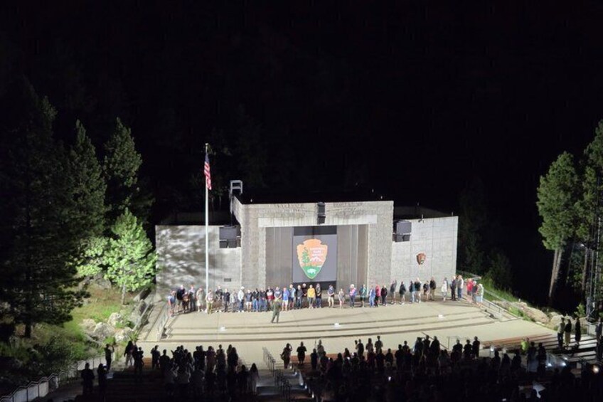 A nighttime outdoor event with a crowd gathered in front of a building with a large emblem on its facade. 5
