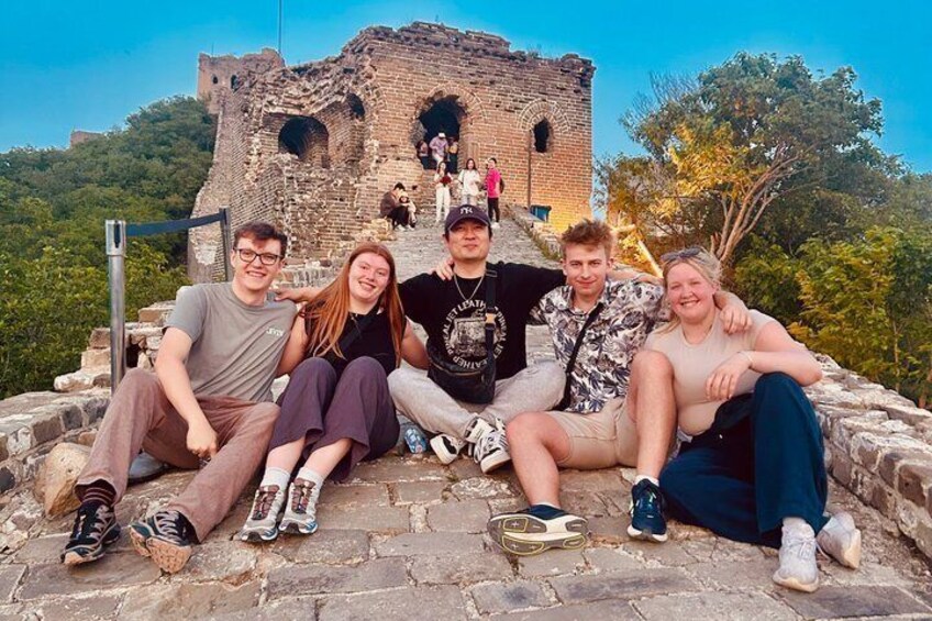 A group of people sitting on a stone platform with the Great Wall of China in the background. 1