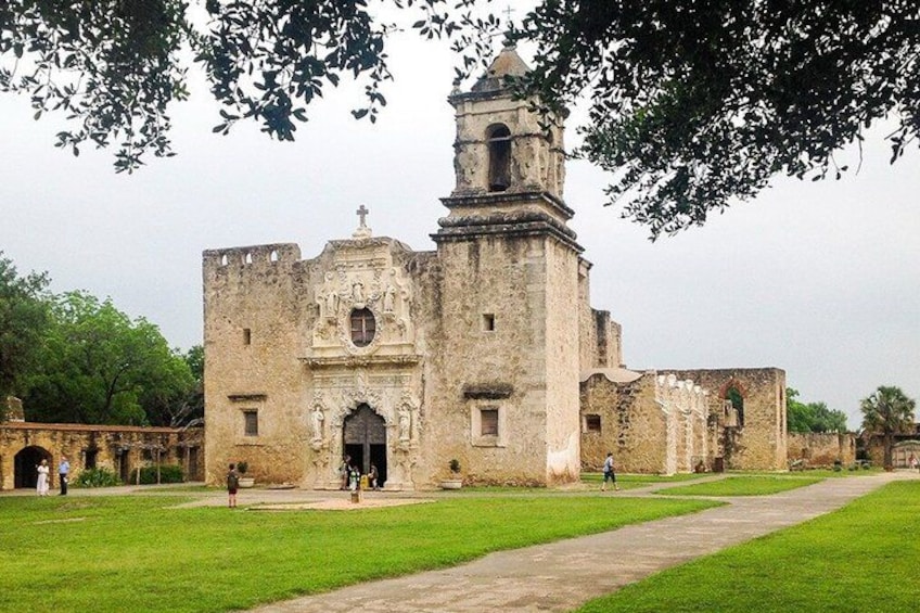An old stone building with a bell tower, surrounded by a grassy area and trees. 4