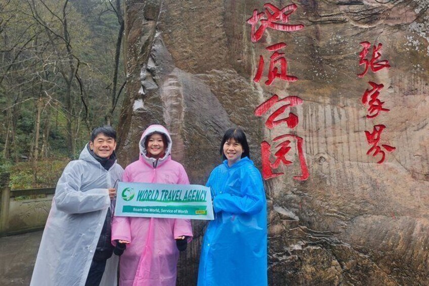 Tres personas sosteniendo un letrero con 'WORLD TRAVEL AGENCY' y una gran roca con caracteres chinos. 4