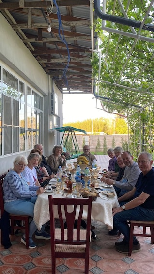 A group of people seated around a table outdoors, engaged in a meal. 4