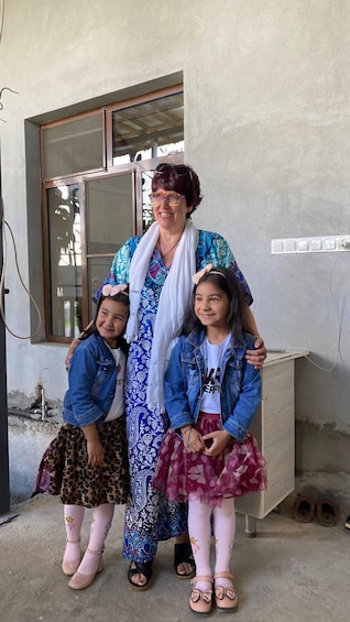 A woman and two children standing in front of a building with a window and a wall socket. 2
