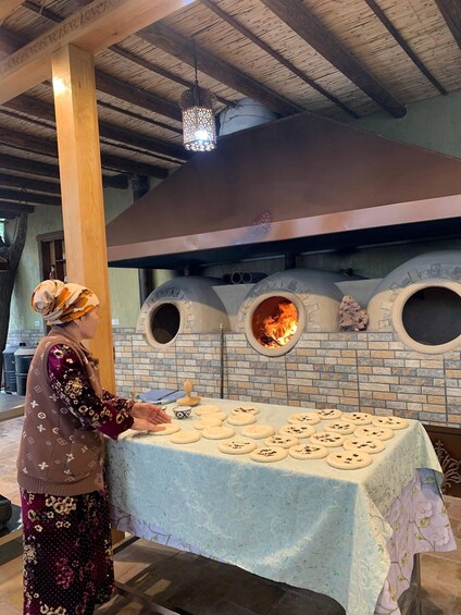 A person at a table with dough, in front of a brick oven with a fire inside. 4