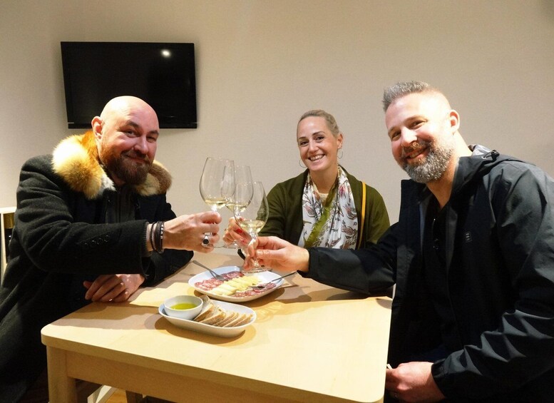 Three people toasting with wine glasses at a table with food. 3