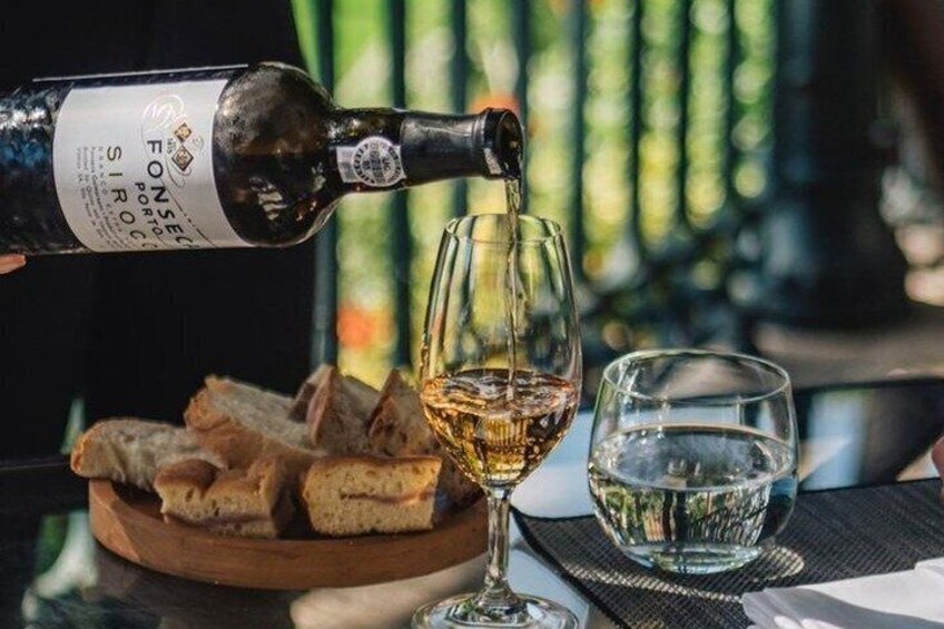 A bottle of wine being poured into a glass, with bread and a water glass on a table. 3