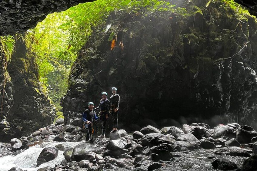 A group of people standing on rocks near a cave entrance with lush greenery. 4