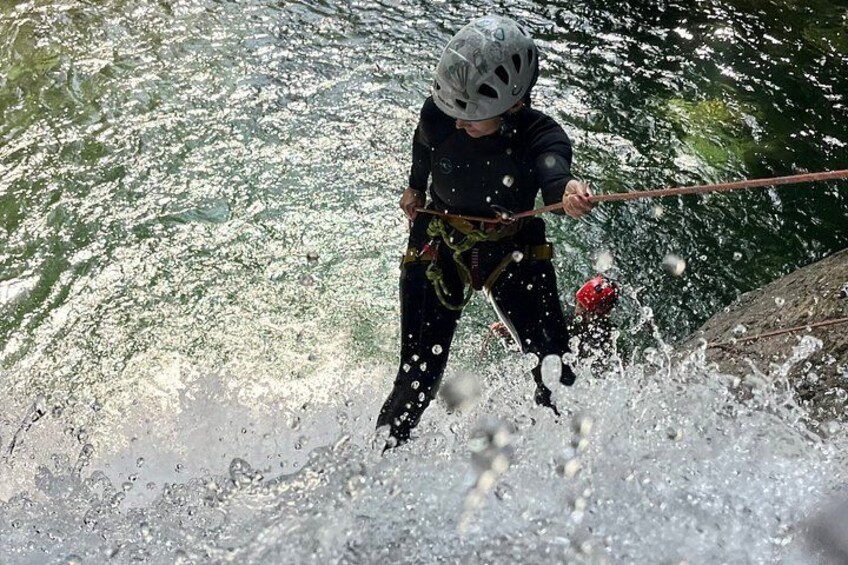 A person rappelling down a water body, wearing a helmet and harness. 1