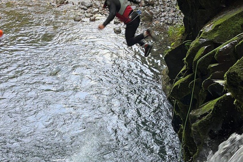 A person wading through a shallow stream with rocks and moss-covered rocks on the right. 2