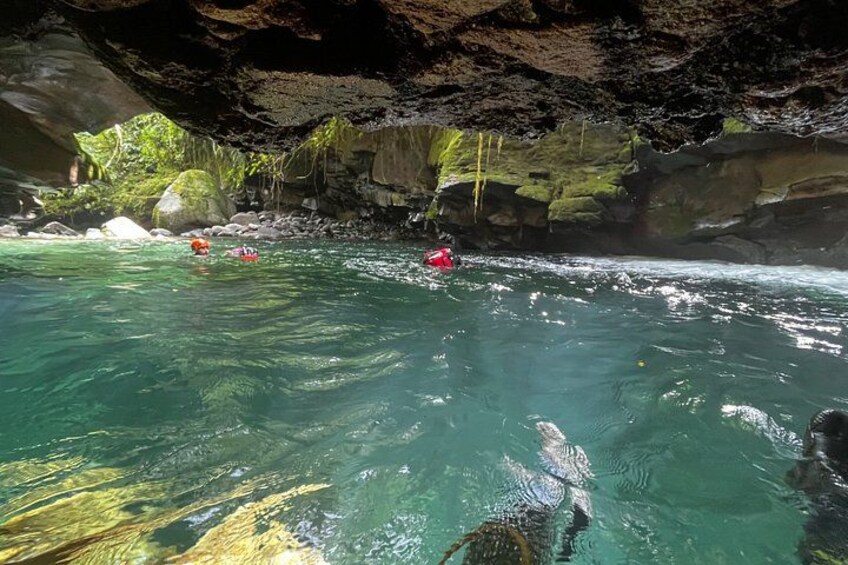 A river with kayaks, clear water, and a rocky cave entrance. 5