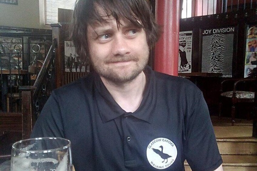 A person sitting at a table with a glass of beer, wearing a black shirt with a logo. 3