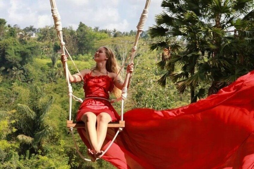 A person in a red dress sitting on a swing with a red canopy, surrounded by lush greenery. 1