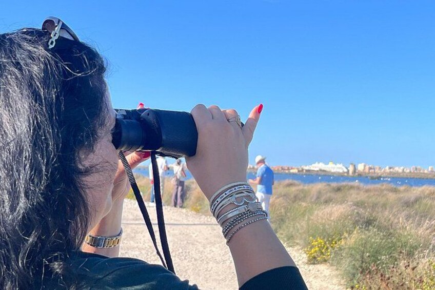 Iemand gebruikt verrekijkers, een horloge en armbanden, met een strand en mensen op de achtergrond. 3