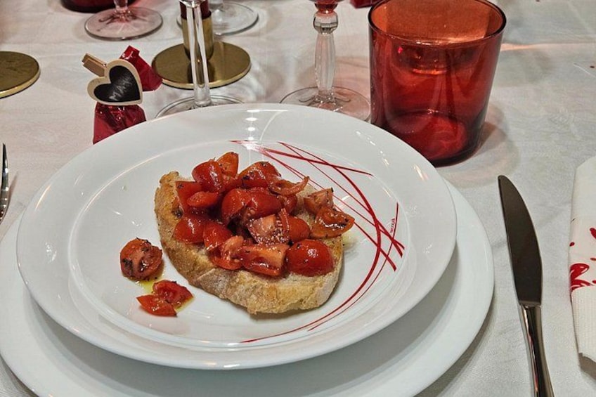 A plate with a slice of toast topped with tomatoes and bacon, a red glass, and a heart-shaped decoration on the table. 4