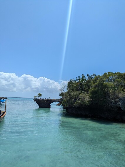 Ein klarer, blauer Himmel, ein Boot auf ruhigem türkisblauem Wasser und eine natürliche Felsformation mit Vegetation. 5