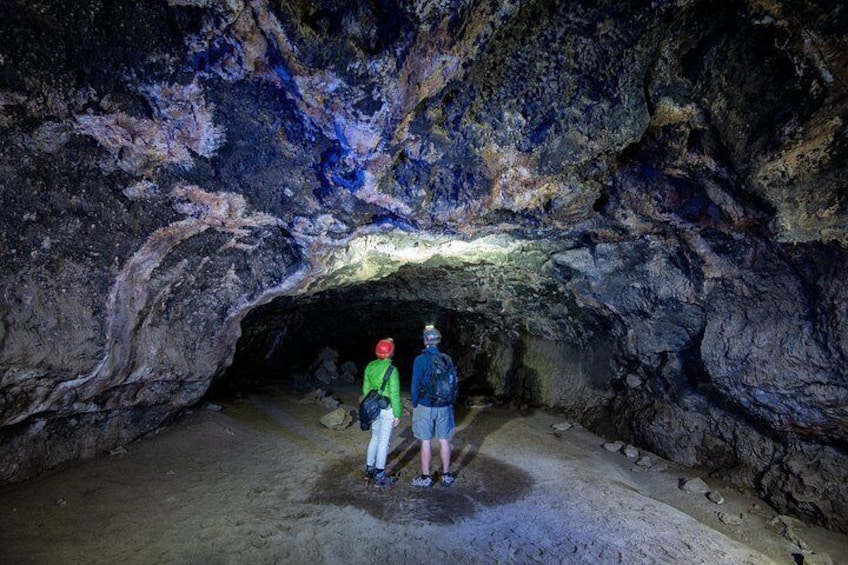 Two people standing in a cave with a rocky ceiling and a narrow passageway. 2