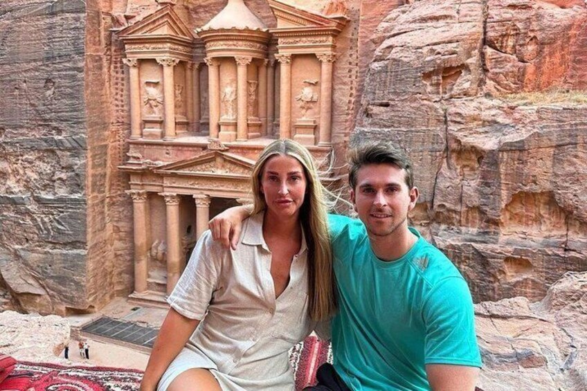 Un couple est assis devant une façade rocheuse sculptée, ornée de colonnes et d’une structure centrale. 2