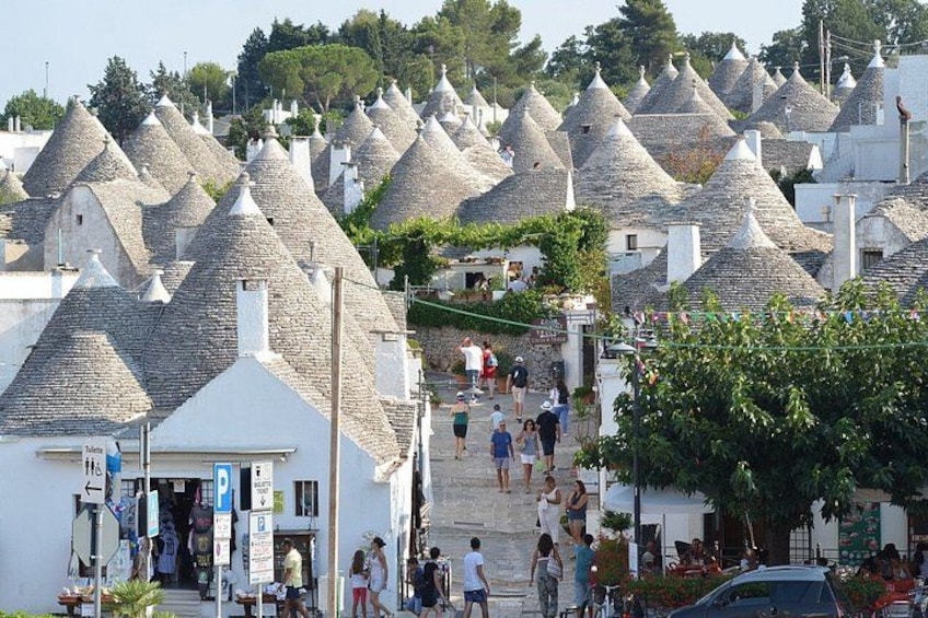 Un villaggio con case a tetti conici, una strada lastricata e persone che passeggiano. 5