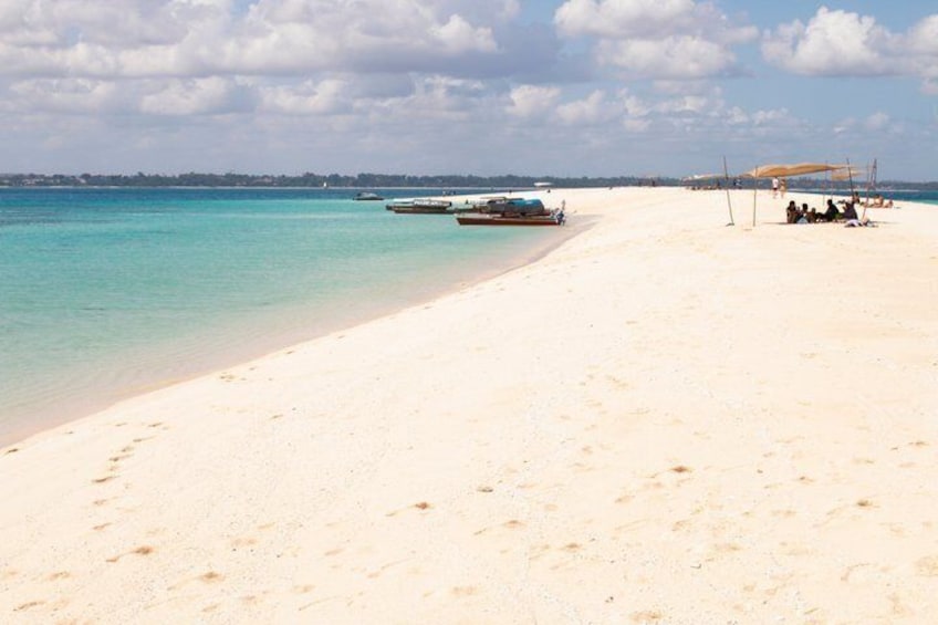 Una spiaggia con acque turchesi cristalline, una riva sabbiosa e alcune barche ancorate. 2
