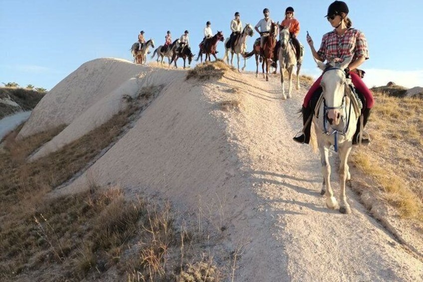 A group of people riding horses on a dirt path with a sandy hill in the background. 2