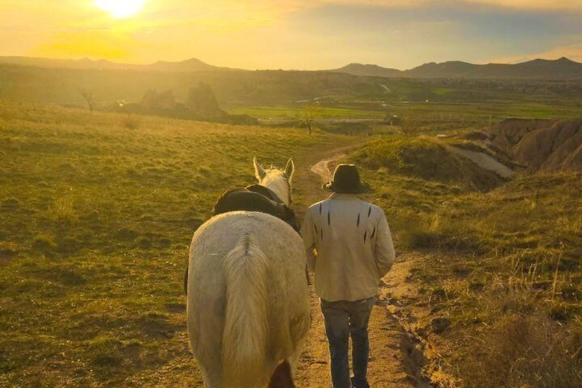 Two people walking a horse on a dirt path with a sunset in the background. 5