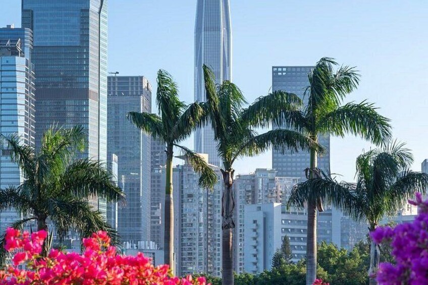 Bybillede med høje bygninger, palmer og lyserøde blomster. 3