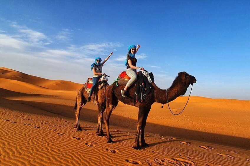 Dos personas montando camellos en un desierto con dunas de arena. 1