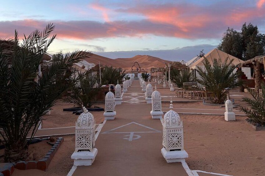 Un resort en el desierto con un camino bordeado de faroles blancos, palmeras y tiendas. 3