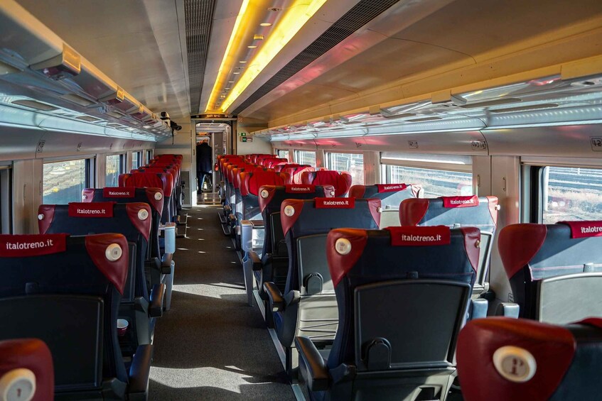 A train interior with rows of red and black seats, overhead luggage compartments, and windows. 4