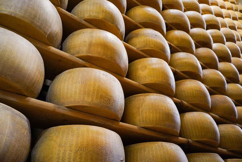 A collection of large, round cheese wheels stacked in rows. 2