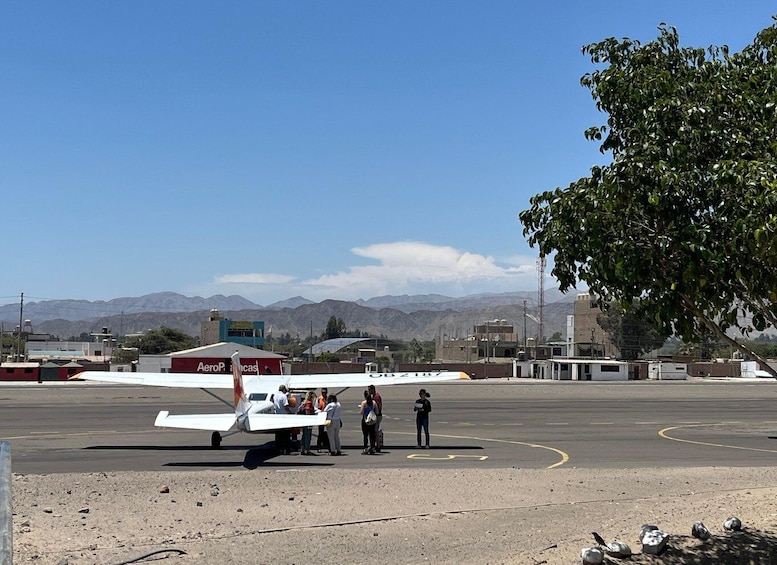 A small white airplane parked on a tarmac with a mountainous backdrop. 1