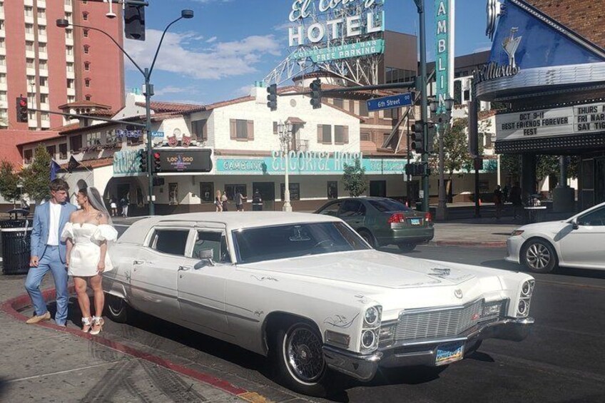 Une voiture blanche ancienne est garée dans une rue de la ville, avec des immeubles et un hôtel en arrière-plan. 2